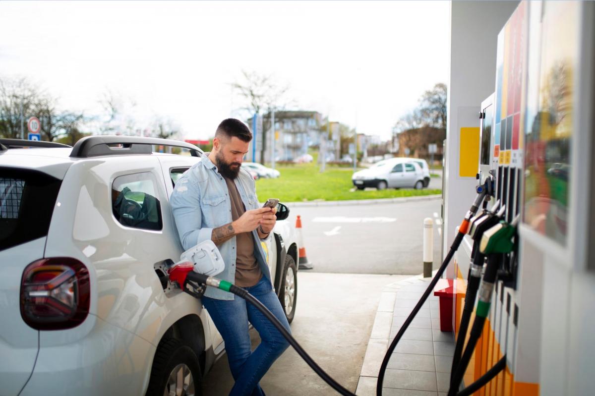 Man steht an der Tankstelle, tankt sein Fahrzeug und checkt dabei das Handy